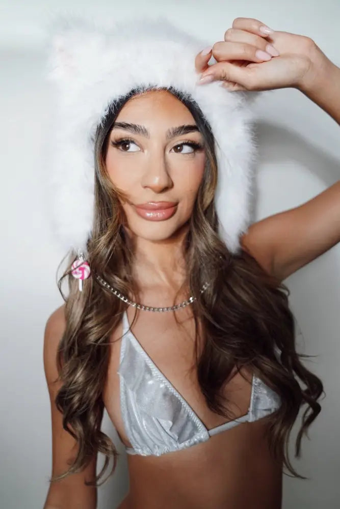 Woman wearing a white fur cat hat and silver bikini top against a plain background