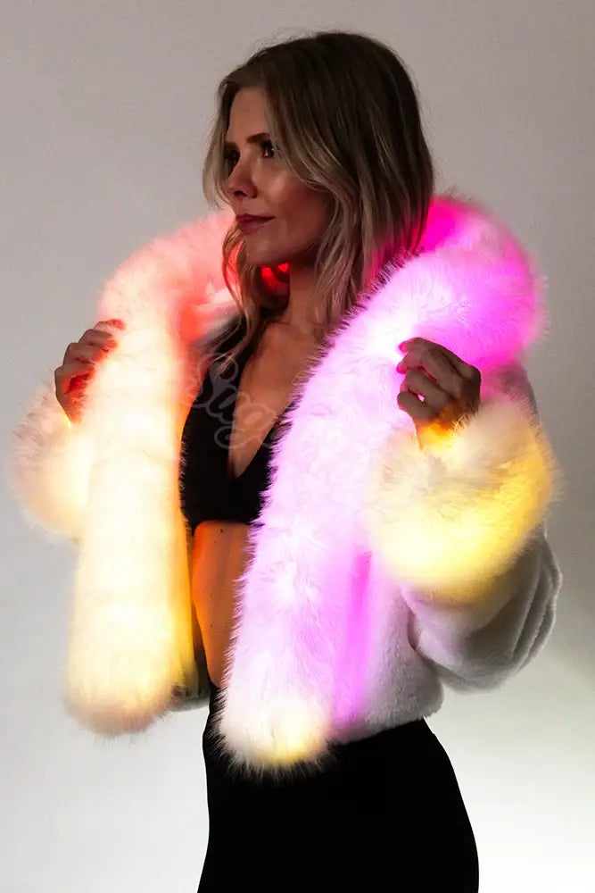 White faux fur light-up festival jacket glowing with colorful LEDs in pink and sunset tones.