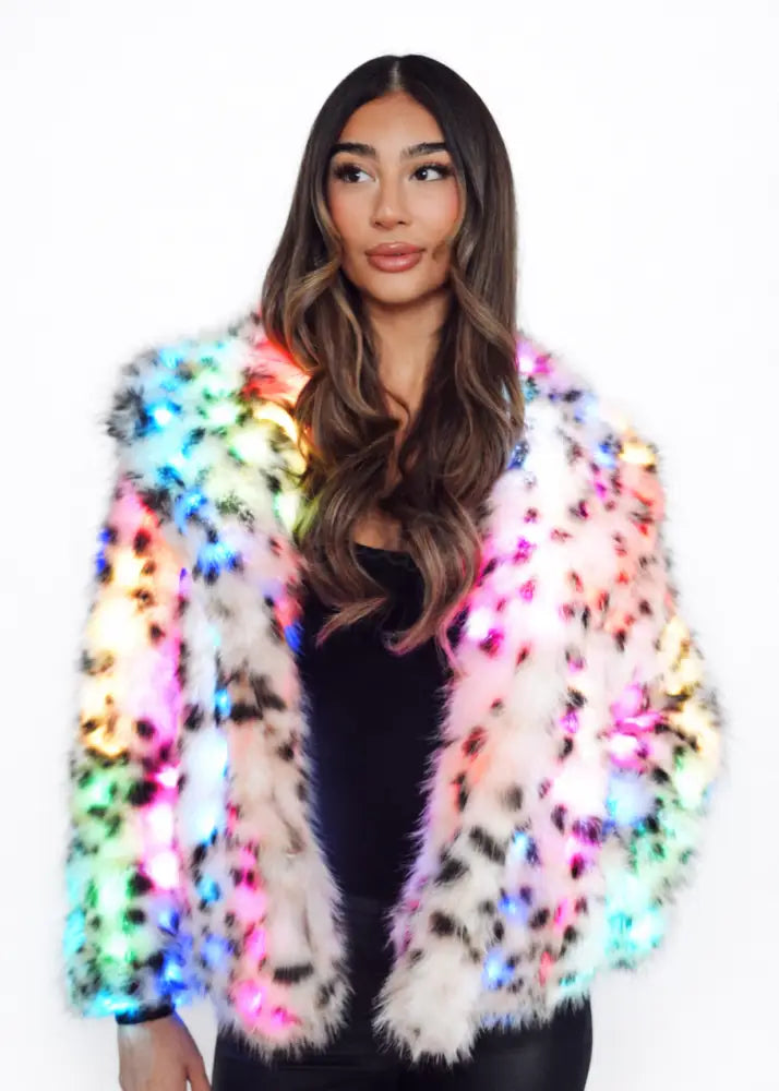 Woman wearing a colorful, illuminated fur led leopard coat against a white background
