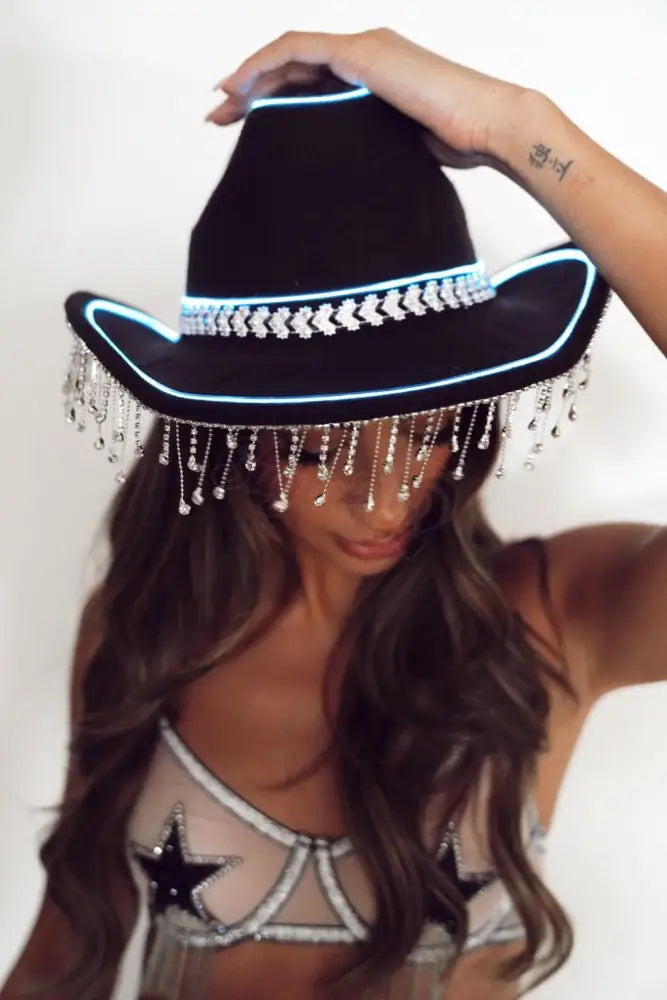 Person wearing a black LED cowboy hat with fringe on a white background