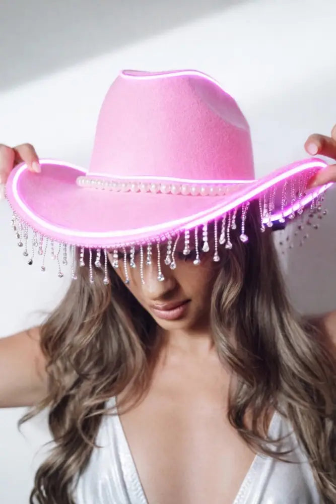 Pink cowboy hat with LED lights held by a person against a white background