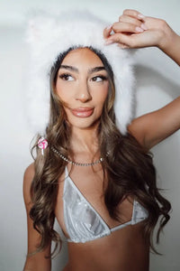 Woman wearing a white fur cat hat and silver bikini top against a plain background