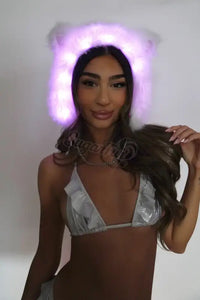 Woman wearing a led fur hat and silver bikini top against a plain background