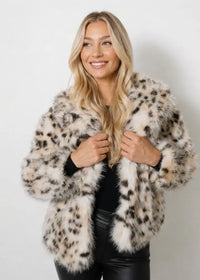 A woman modeling a fluffy faux fur jacket with a beige, brown, and black leopard print pattern, paired with a black top and black pants, against a plain light gray background.